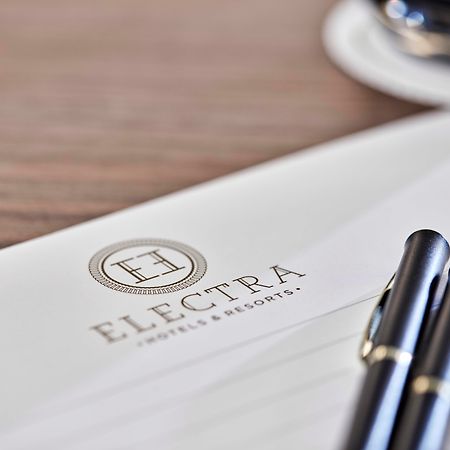 Electra Metropolis Hotel Athena Bagian luar foto The photo shows a letterhead or stationery featuring the logo of "Electra Hotels & Resorts." The logo includes a stylized letter "H" enclosed in a circle. There are two black pens positioned on the paper, and a glimpse of a cup, likely with coffee, i