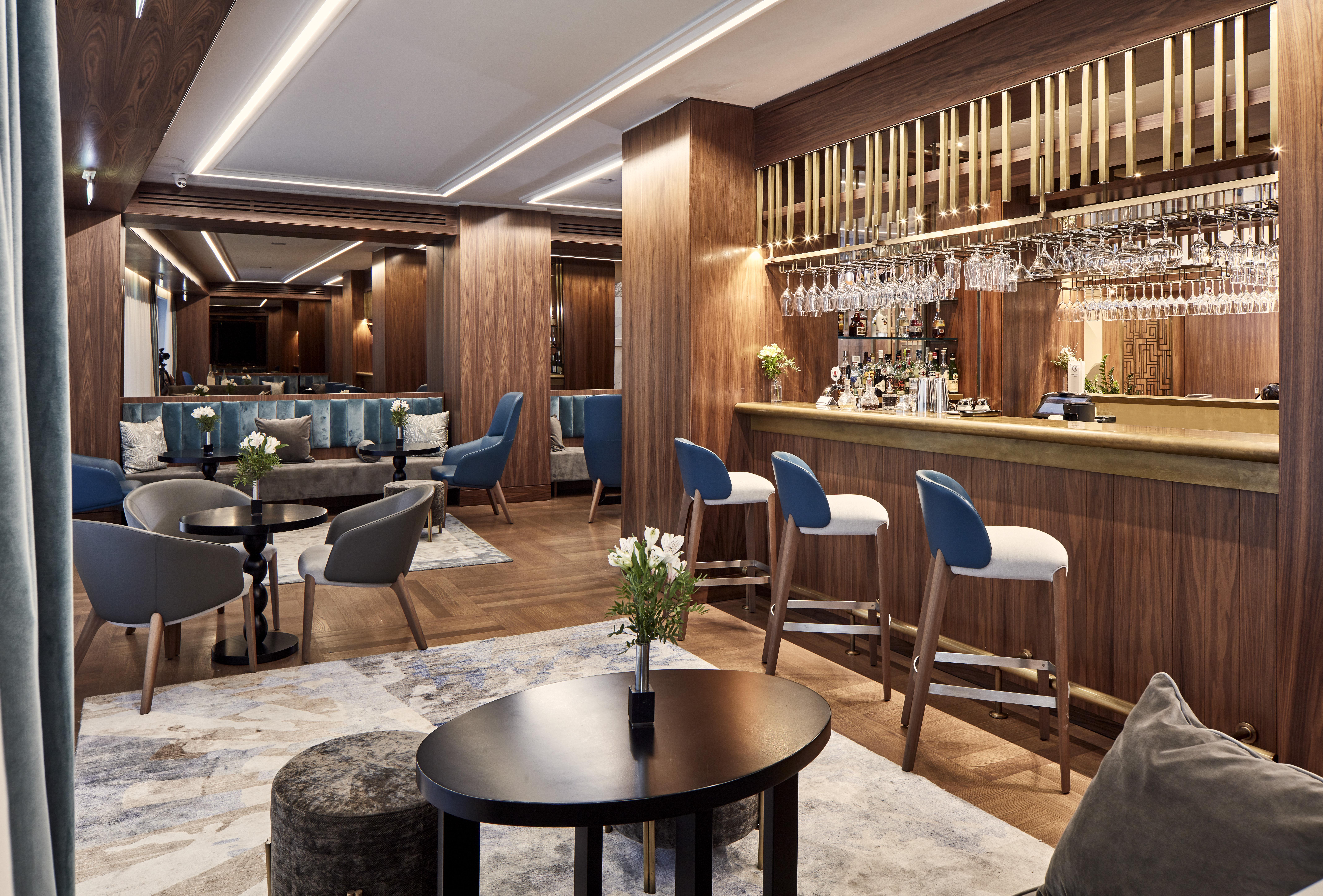 Electra Metropolis Hotel Athena Bagian luar foto The photo shows an elegant bar or lounge area featuring a modern design. The space is adorned with rich wooden paneling and stylish furnishings. There is a bar with a brass countertop, behind which various bottles and glassware are displayed. Seating